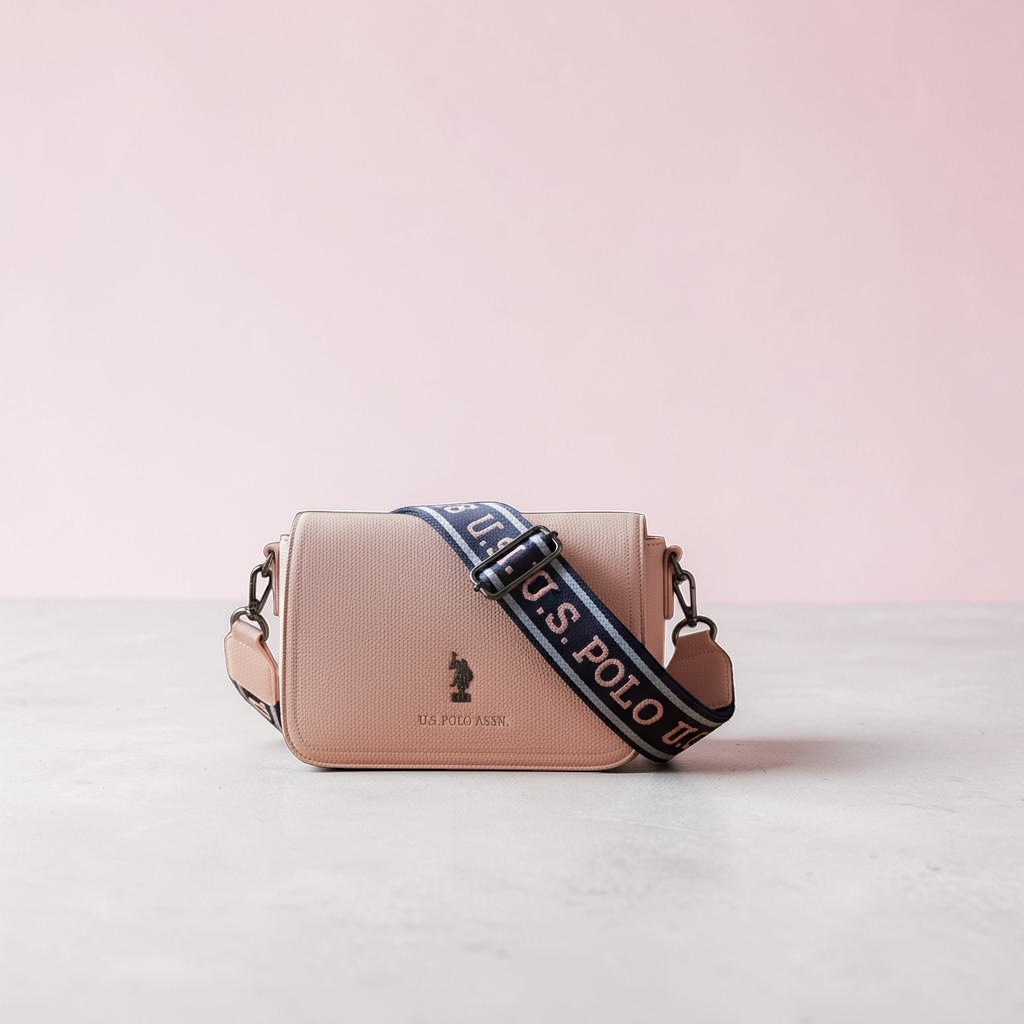 Bolso bandolera rosa www.treshop.com.co con textura, correa ajustable con logo y emblema frontal de U.S. Polo Assn.