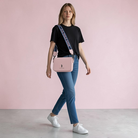 Modelo luciendo bolso bandolera rosa de www.treshop.com.co con correa ancha y logo U.S. POLO ASSN. en fondo rosa