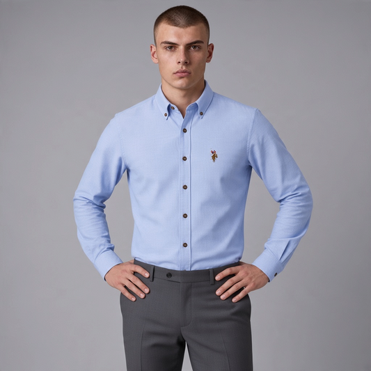 Hombre vistiendo camisa azul claro de manga larga www.treshop.com.co con cuello button-down y logo bordado en pecho