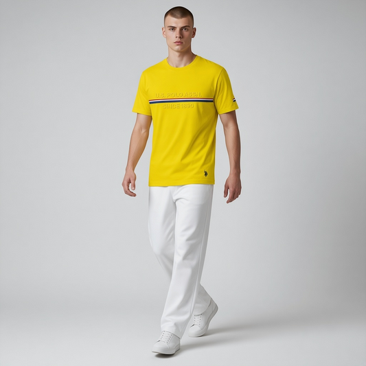 Hombre vistiendo camiseta amarilla de algodón www.treshop.com.co con logo y franja tricolor, combinada con pantalón blanco