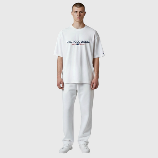 Hombre vistiendo camiseta blanca de algodón U.S. POLO ASSN. con logo frontal y pantalones a juego en www.treshop.com.co