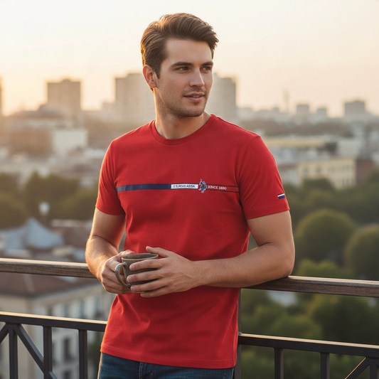 Hombre vistiendo camiseta roja de manga corta www.treshop.com.co con logo y franja horizontal en una terraza urbana