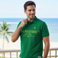 Hombre vistiendo polo verde U.S. Polo Assn. con estampado hawaiano y logo bordado en un entorno de playa tropical