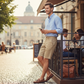 Hombre con bermudas beige U.S. POLO ASSN. de www.treshop.com.co, camisa azul y mocasines en una terraza urbana.