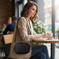 Mujer con bolso bandolera negro U.S. Polo Assn. de www.treshop.com.co con correa tejida y logo en cafetería