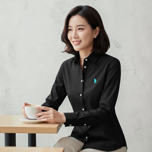 Mujer vistiendo camisa formal negra de manga larga U.S. Polo Assn. con logo azul bordado, sentada en una mesa.