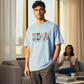 Hombre vistiendo camiseta azul claro de algodón U.S. Polo Assn. con estampado gráfico frontal en un salón moderno.