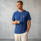 Hombre vistiendo camiseta azul de algodón www.treshop.com.co con logo bordado y detalles tricolores en cuello y bajo