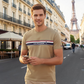 Hombre con camiseta beige de algodón www.treshop.com.co con franja horizontal y logo bordado en una calle de París