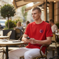 Hombre con camiseta roja de algodón U.S. Polo Assn. con cuello redondo y logo gráfico sentado en una terraza