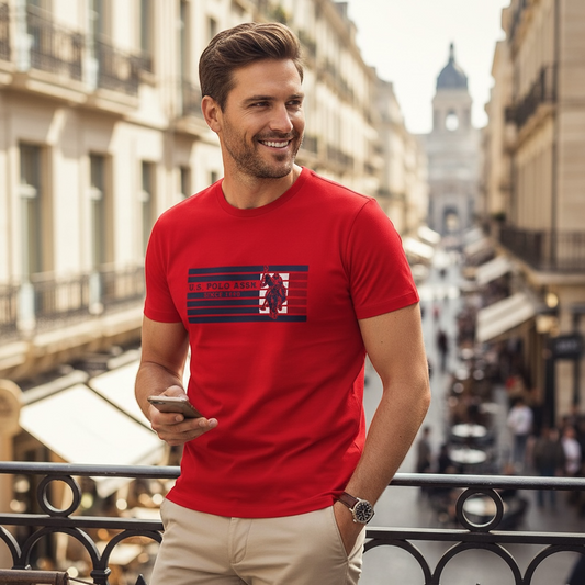 Hombre sonriente vistiendo camiseta roja de algodón U.S. Polo Assn. con logo y franjas azules en entorno urbano
