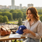Mujer sosteniendo una gorra azul USPA con logo bordado blanco en una terraza con vista a la ciudad de www.treshop.com.co