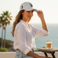 Mujer con gorra blanca www.treshop.com.co con bordado azul marino y numero tres lateral en terraza frente al mar
