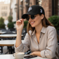 Mujer con gorra negra www.treshop.com.co con bordado de polo y numero 3 lateral, estilo casual en terraza urbana.