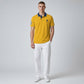 Hombre vistiendo polo amarillo mostaza www.treshop.com.co con cuello azul marino, logo bordado y pantalón blanco