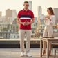 Hombre vistiendo polo rojo con franjas de www.treshop.com.co junto a mujer en terraza urbana al atardecer