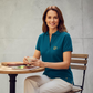 Mujer sonriente vistiendo polo azul petróleo U.S. Polo Assn. de www.treshop.com.co con logo dorado en mesa de café