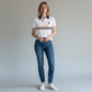 Mujer vistiendo polo blanco www.treshop.com.co con cuello azul marino, logo y franjas, combinado con jeans azules.