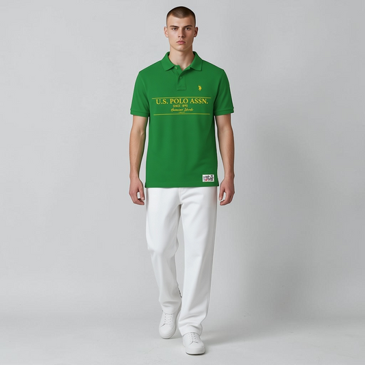 Polo verde de algodón www.treshop.com.co con estampado amarillo y logo bordado, usado por un modelo con pantalón blanco